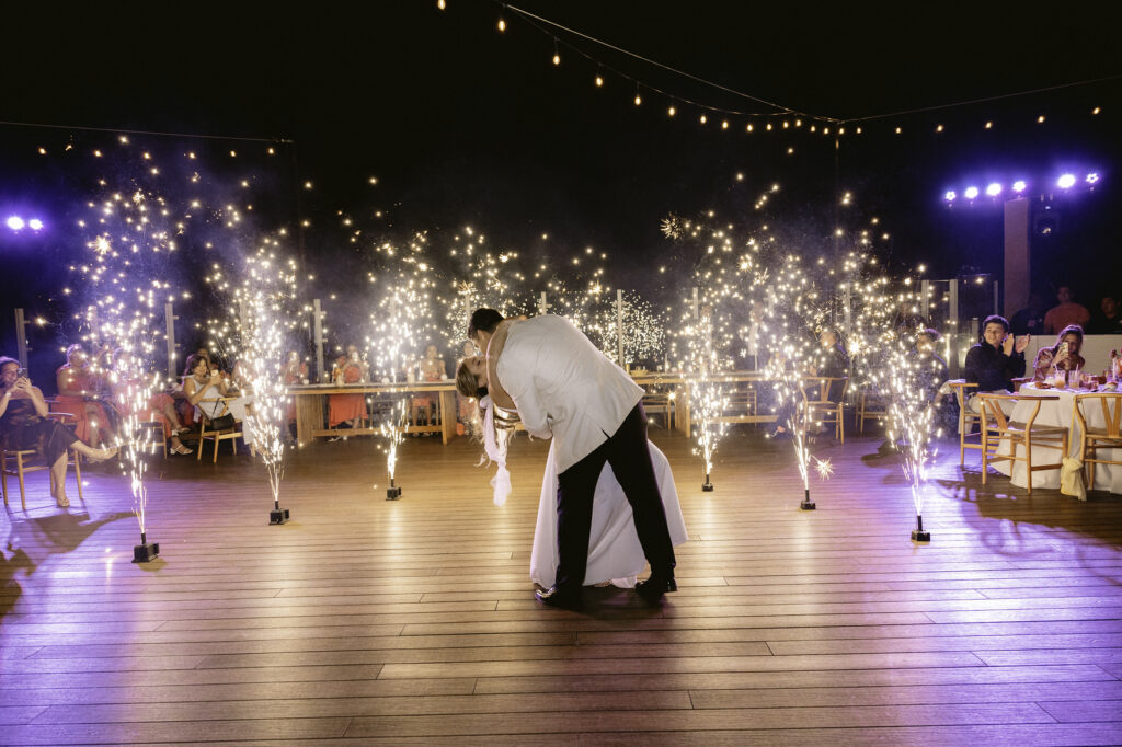 bride and groom dancing first dance on a wooden dancefloor with fireworks on Cabo Corazon Rooftop Wedding Venue in Mexico